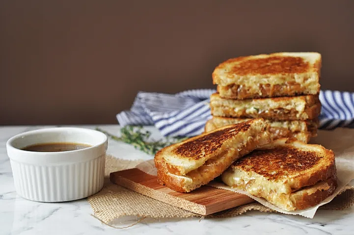 a stack of grilled cheese halve sandwiches next to a cup of sipping sauce