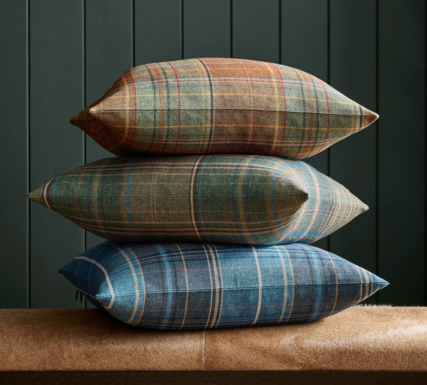 An up close image of a stack of three plaid print pillows on a sofa or stool