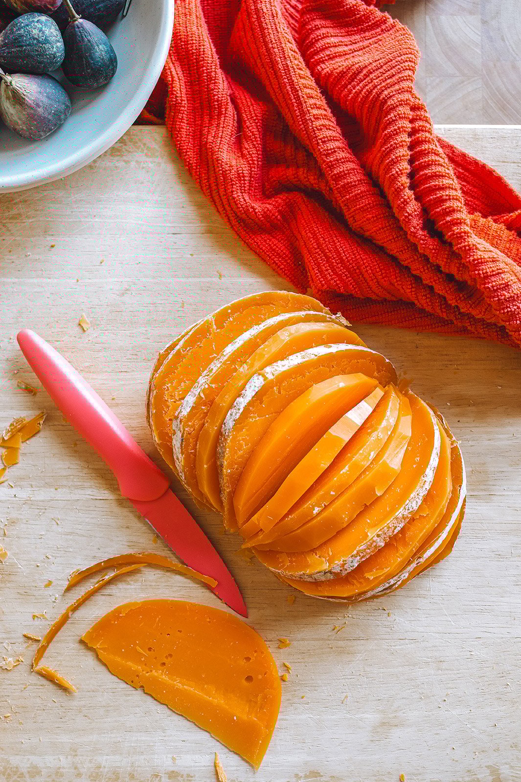 A ball of Mimolette cheese on a cutting board fanned out into slices that resemble the shape of a pumpkin