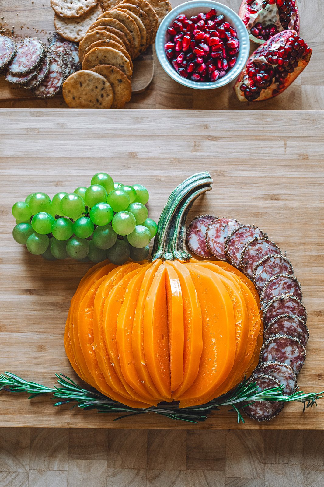 A charcuterie board with Mimolette cheese cut in the shape of a pumpkin surrounded by crackers, meat, grapes, cranberries, olives, and sardines