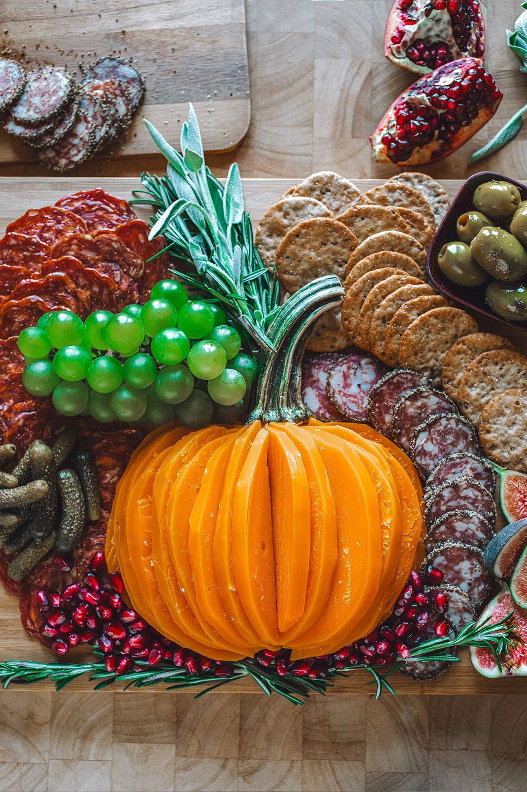 A charcuterie board with Mimolette cheese cut in the shape of a pumpkin surrounded by crackers, meat, grapes, cranberries, olives, and sardines