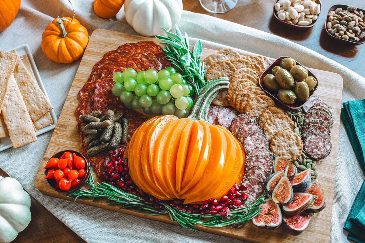 A charcuterie board with Mimolette cheese cut in the shape of a pumpkin surrounded by crackers, meat, grapes, cranberries, olives, and sardines
