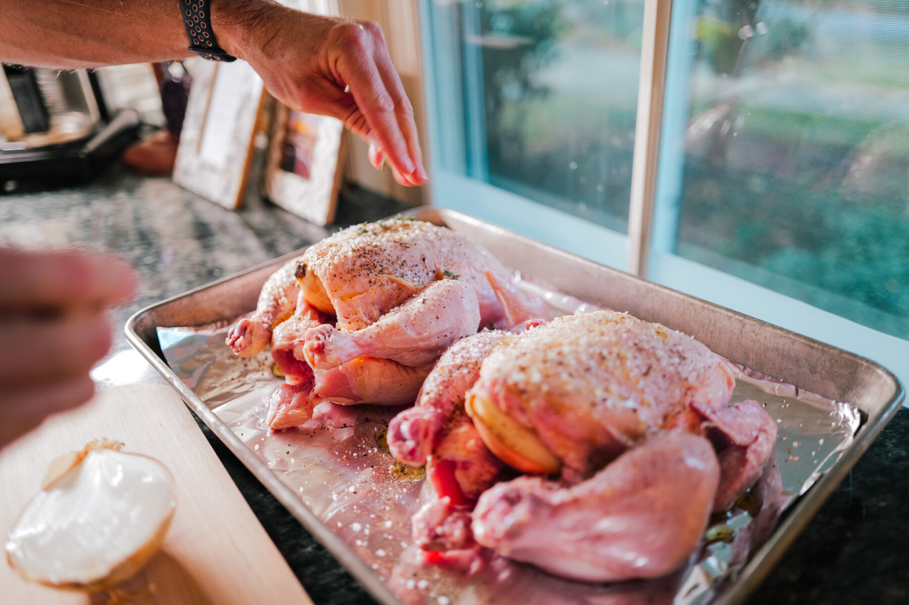 Sprinkling seasoning over two whole chickens before roasting