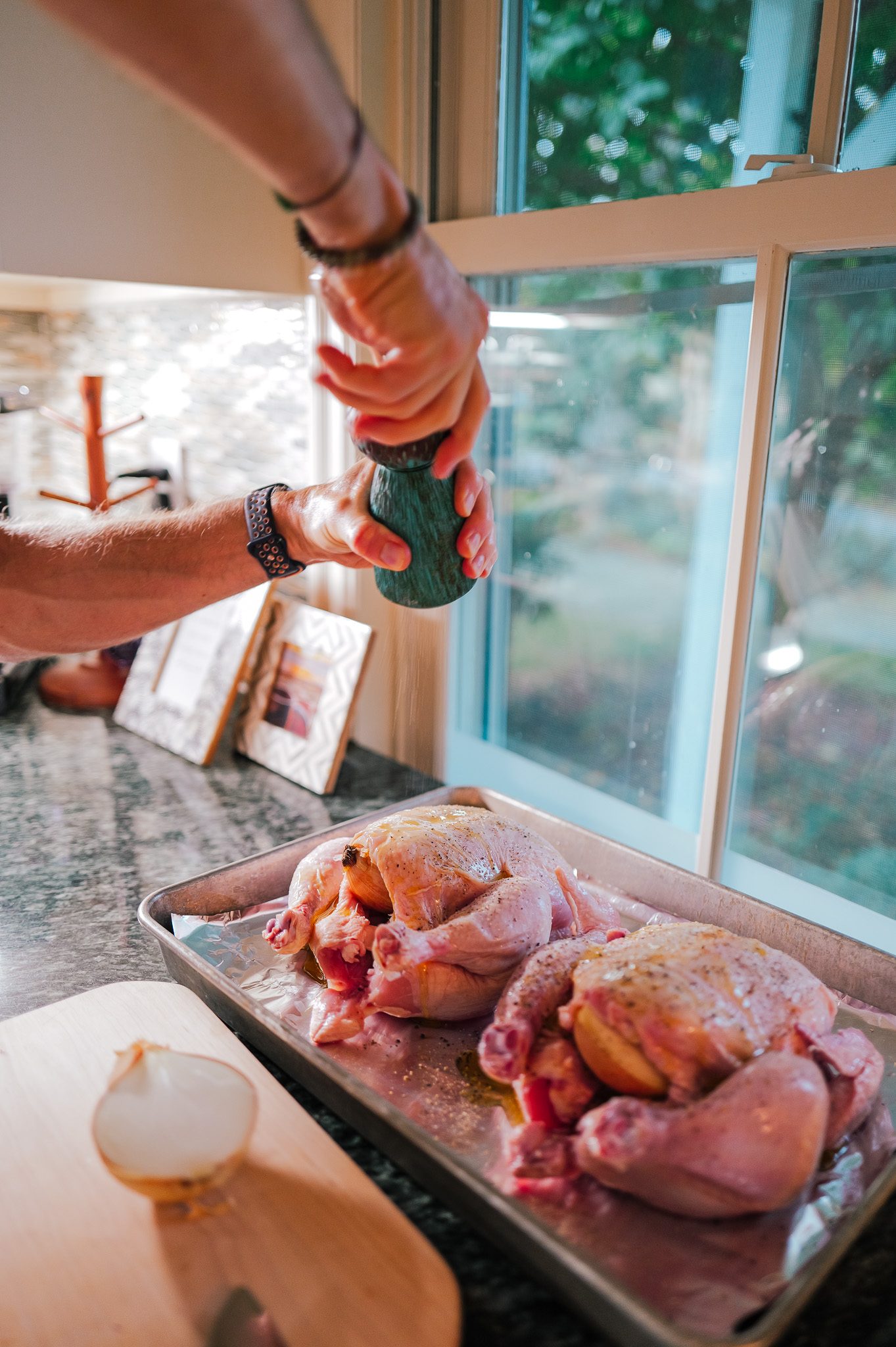 Grinding pepper over whole chickens on a foil-lined sheet pan